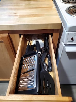 A drawer with kitchen utensils including a grater and spatulas.