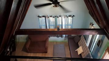 A room with a ceiling fan, a sofa, a chair, and a window with curtains.