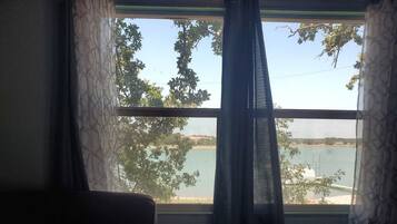 A room with a view of a body of water, a window with curtains, and a sofa.