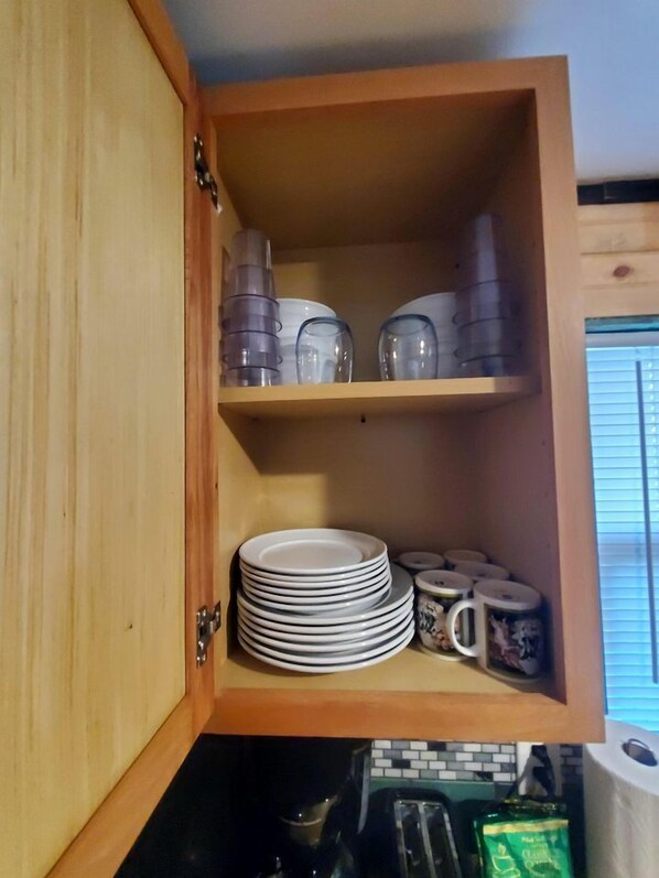 A wooden cabinet with shelves containing plates, cups, and a coffee maker.