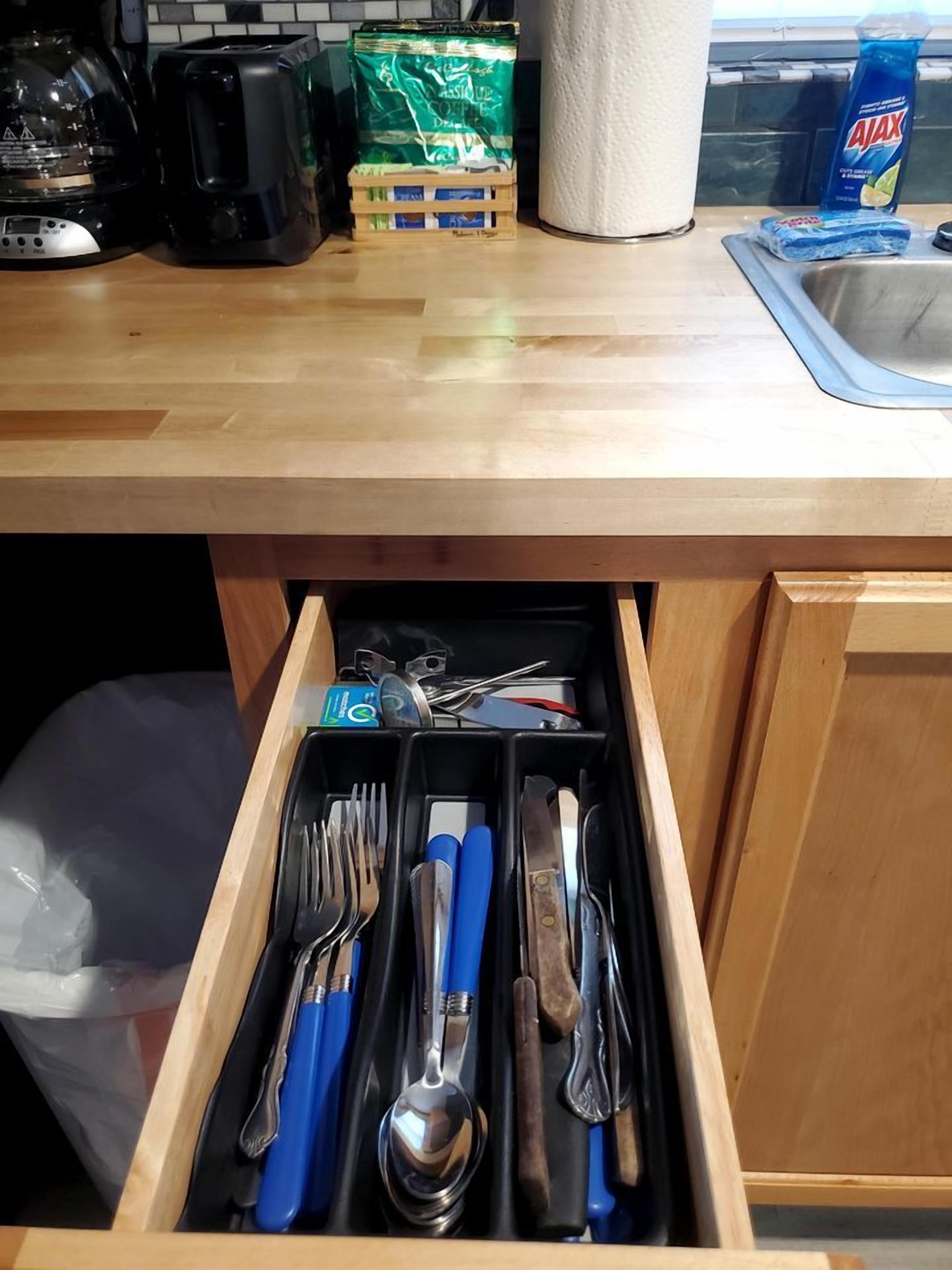 A kitchen with a drawer containing utensils, a coffee maker, a toaster, and a bag of coffee.