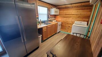 A compact kitchen with wooden walls, a stainless steel refrigerator, a microwave, a sink, and a dining table.