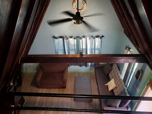 A room with a ceiling fan, a sofa, a chair, and a window with curtains.
