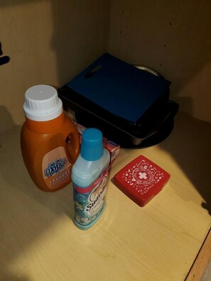 A wooden shelf with a blue container, a bottle of OxyClean, a bottle of Swiffer, and a red box with a white cross.