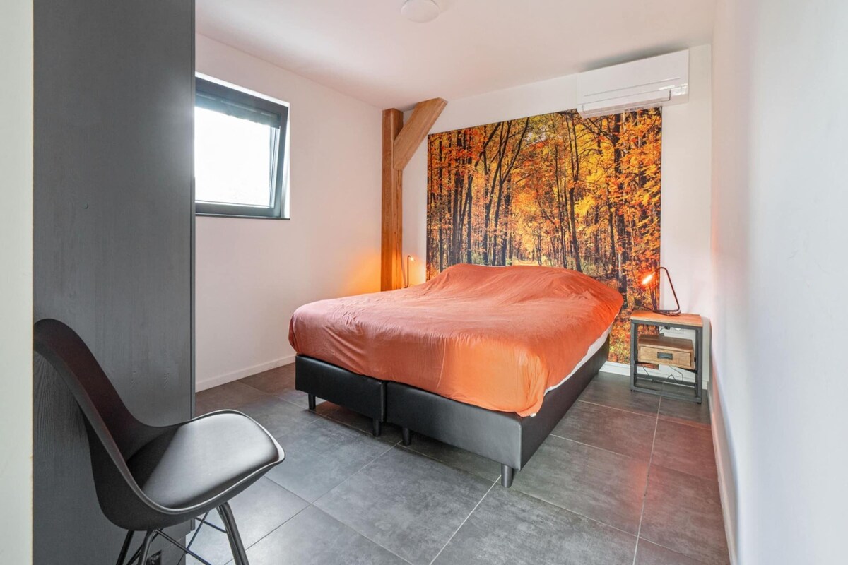 A bedroom with a bed, a chair, a nightstand, a window, and a wall with a forest mural.