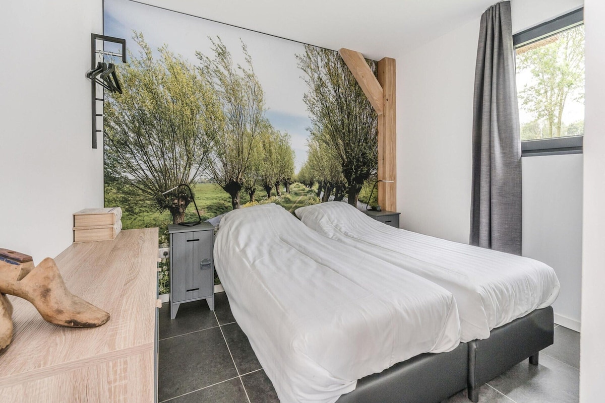 A bedroom with a bed, a desk, a chair, a wardrobe, and a large window with curtains.