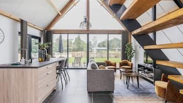 A modern kitchen with a large island, a dining area with a sofa and chairs, and a view of the outdoors through large windows.