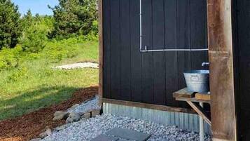 A small, dark-colored outdoor structure with a metal showerhead and a metal basin.