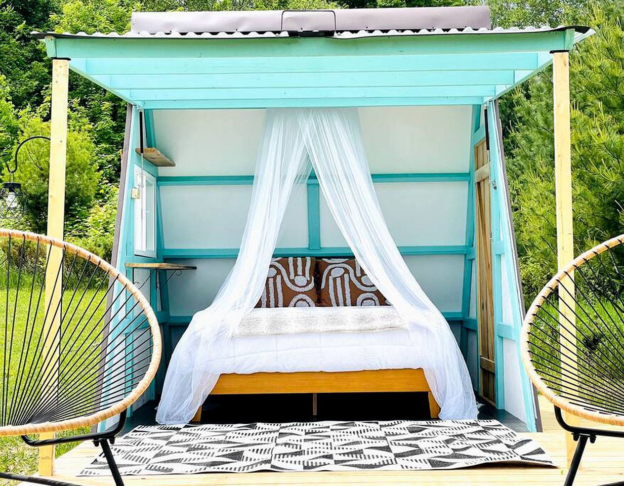 A single bed with a canopy in an outdoor setting, surrounded by greenery.