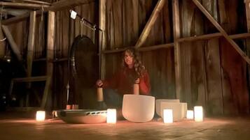 A rustic interior with wooden beams, a large white bowl, and several lit candles on a wooden floor.