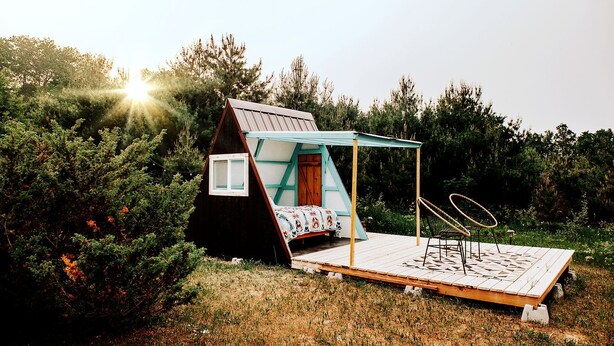 A small, A-frame wooden cabin with a bed and a deck.