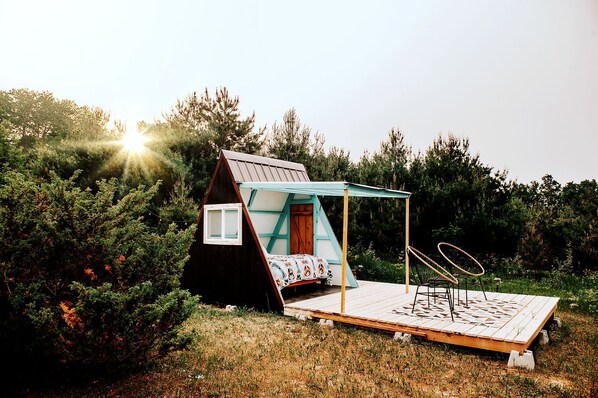 A small, A-frame wooden cabin with a bed and a deck.