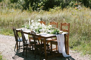 A wooden table set outdoors with chairs, surrounded by natural vegetation. - A-Frame Serenity: Tiny Cabin with Panoramic Scenery in Michigan's Tranquil Setting (Boyne Falls)