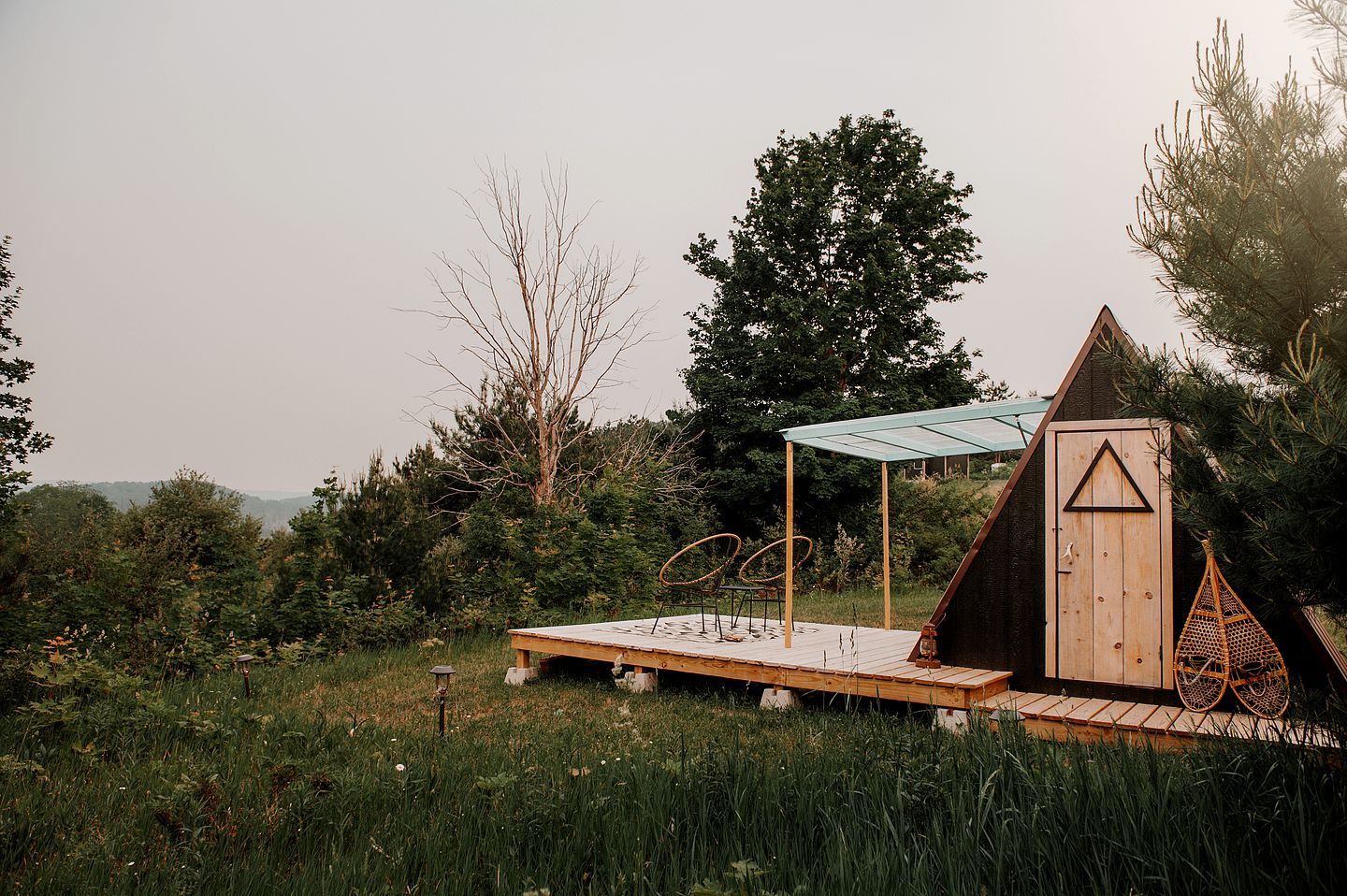 A wooden cabin with a triangular roof, a small porch, and a glass-covered structure.