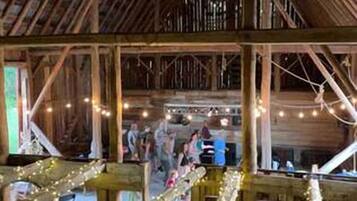 Un intérieur de style rustique, évoquant une grange, avec des poutres en bois, des tables et des guirlandes lumineuses.