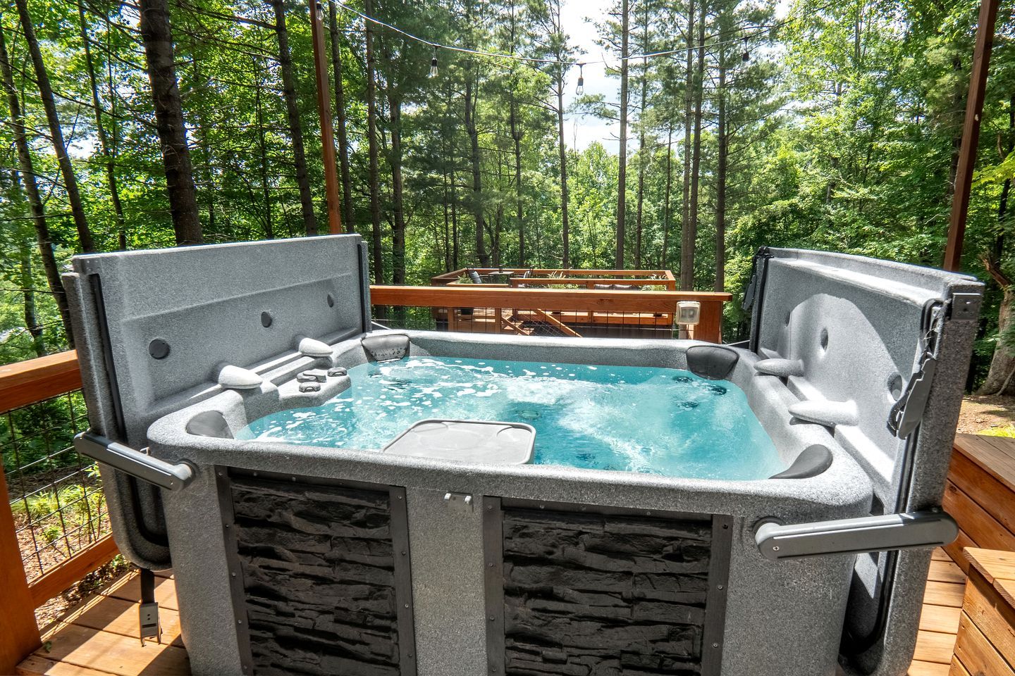 Un jacuzzi en una terraza exterior con barandilla de madera y un muro de piedra.