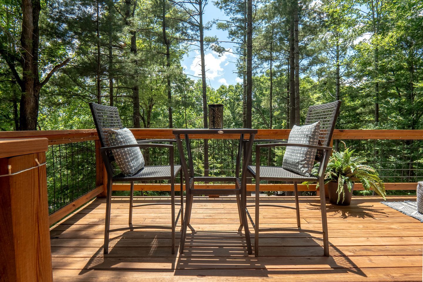 Une terrasse en bois avec deux chaises et une table, entourée d’une forêt.