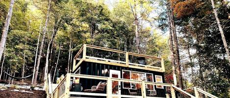 A multi-level wooden cabin with a deck and stairs, surrounded by trees.