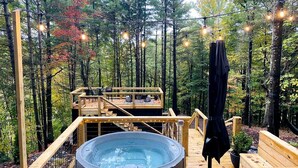 Un jacuzzi en una terraza de madera rodeado de árboles, con una silla y un banco de madera.