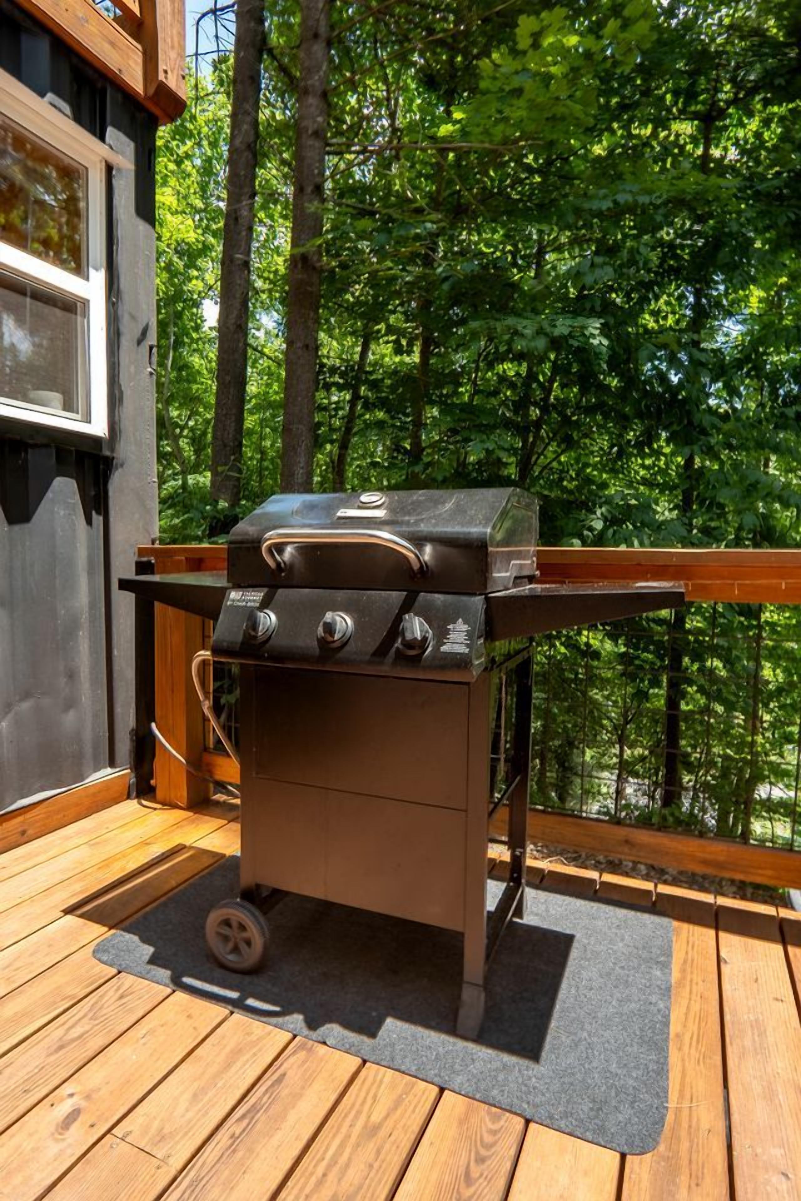 A portable barbecue grill on a wooden deck with a view of a forest.