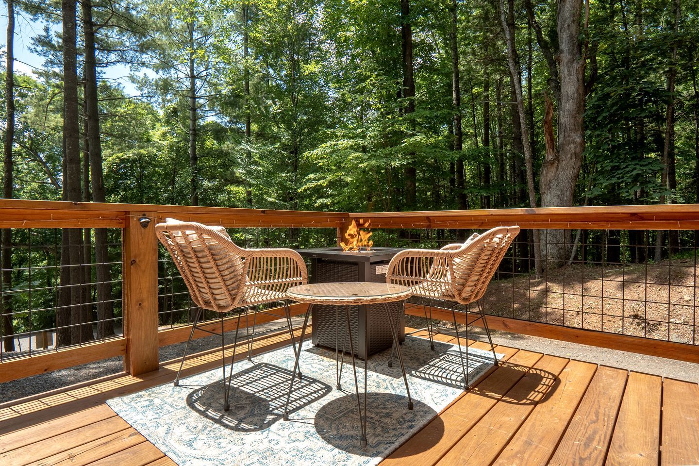 A deck with wicker chairs, a table, and a fire feature.