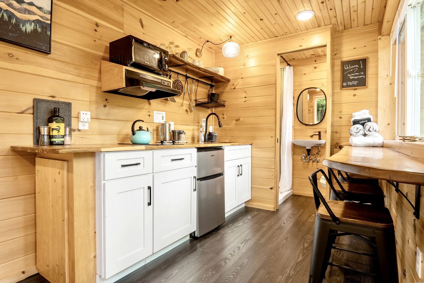 A wooden interior with a kitchen area featuring a dishwasher, a kettle, and a toaster. There is a sink and a mirror on the wall.