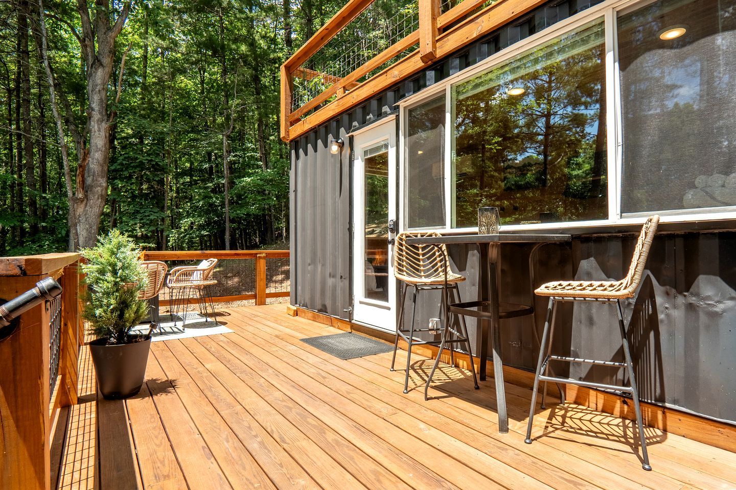 Une terrasse en bois avec deux tabourets de bar en osier et une plante en pot.