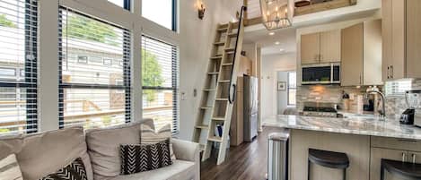 A modern kitchen with a central island, a dining area with a sofa, and a staircase leading to an upper level.