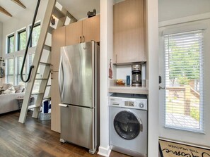 Une cuisine compacte équipée d’un réfrigérateur en acier inoxydable, d’un lave-linge, de meubles en bois et d’une échelle.