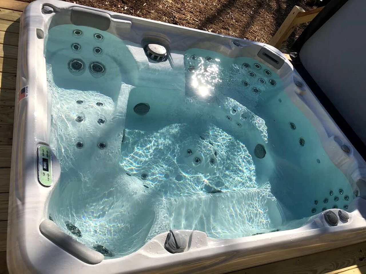Un bain à remous doté de plusieurs jets, d’un panneau de commande et d’une terrasse en bois qui l’entoure.
