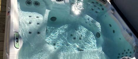 A hot tub with multiple jets, a control panel, and a wooden deck surrounding it.