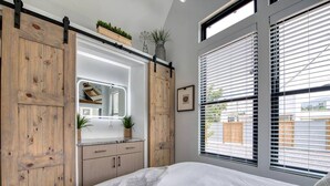 Een slaapkamer met een bed, een dressoir, een spiegel en een raam met jaloezieën.