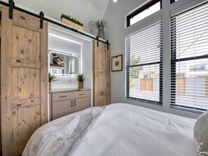 Ein Schlafzimmer mit Bett, Kommode, Spiegel und einem Fenster mit Jalousien.