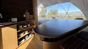 A tented room with a wooden table, shelves with kitchenware, and a view of the outdoors. - Cosmic Intimacy: Geodesic Dome Escape for Couples in a Dreamy Michigan Setting (Boyne Falls)