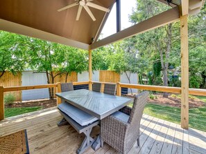 Una terraza techada al aire libre con una mesa y sillas, rodeada por un cerco de madera y árboles.