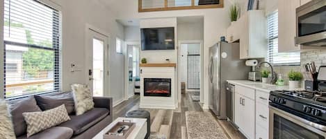 A modern kitchen with a built-in oven, a dining area with a sofa and coffee table, and a fireplace.