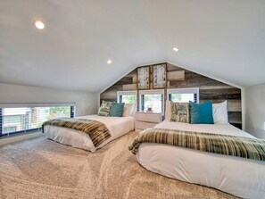 Un dormitorio con dos camas, techo inclinado y ventanas amplias.