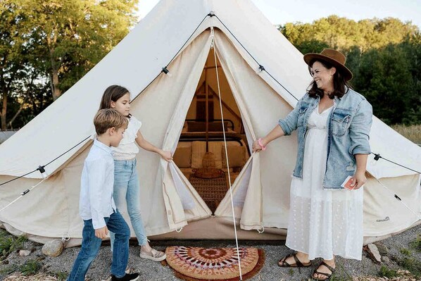 A family of three in front of a large, beige, dome-shaped tent with a visible interior.