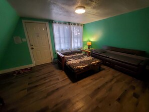A bedroom with a bed, a couch, a door, and a window with curtains.