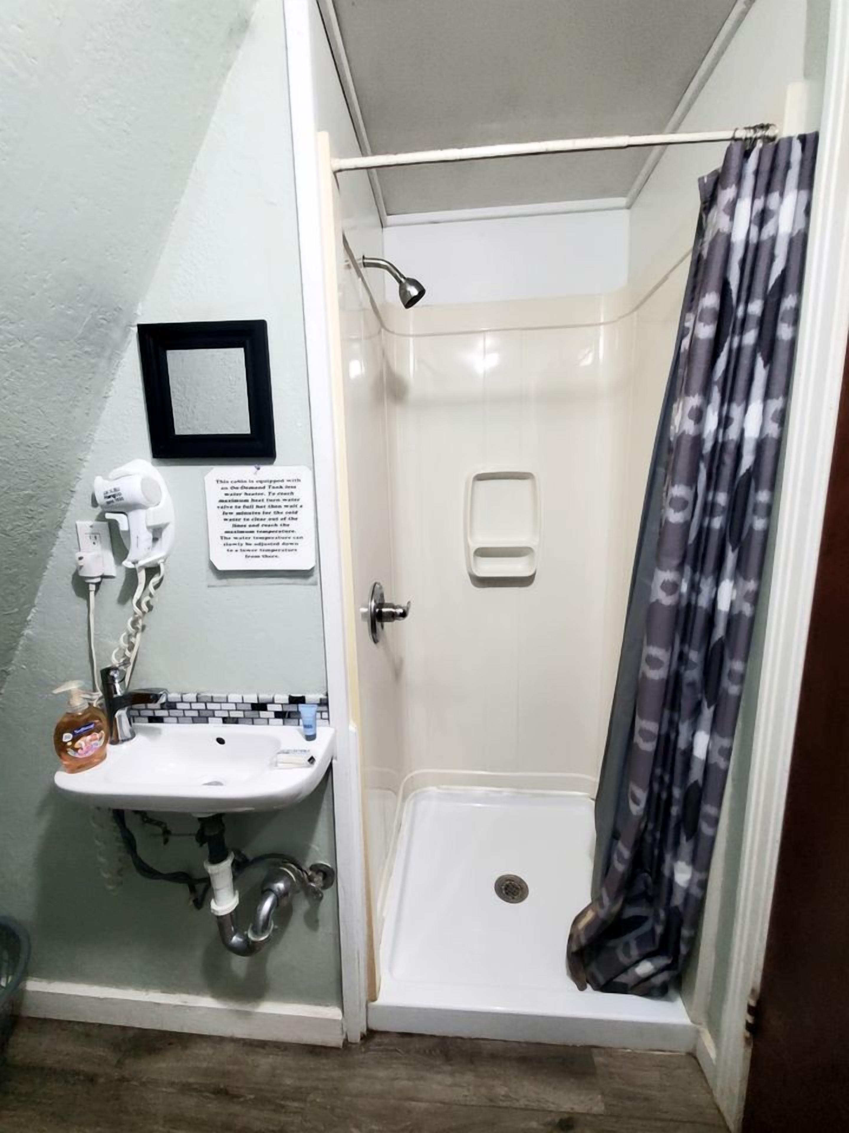 A small bathroom with a shower, a sink, and a mirror.