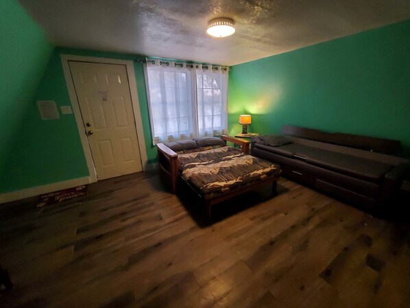A bedroom with a bed, a couch, a door, and a window with curtains.