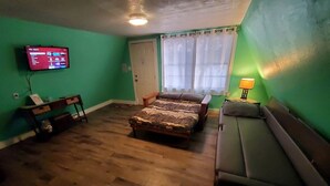 A room with a bed, a sofa, a TV on the wall, and a window with curtains.