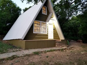 A small, single-story wooden cabin with a gabled roof, a front door, and a window.