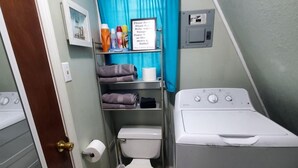 A small bathroom with a toilet, a washing machine, and a shelf with toiletries.
