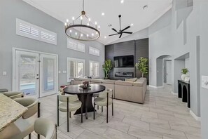 A modern living room with a dining area, a large TV, and a ceiling fan. - Stylish Family Getaway | Fully Furnished Home (Las Vegas)