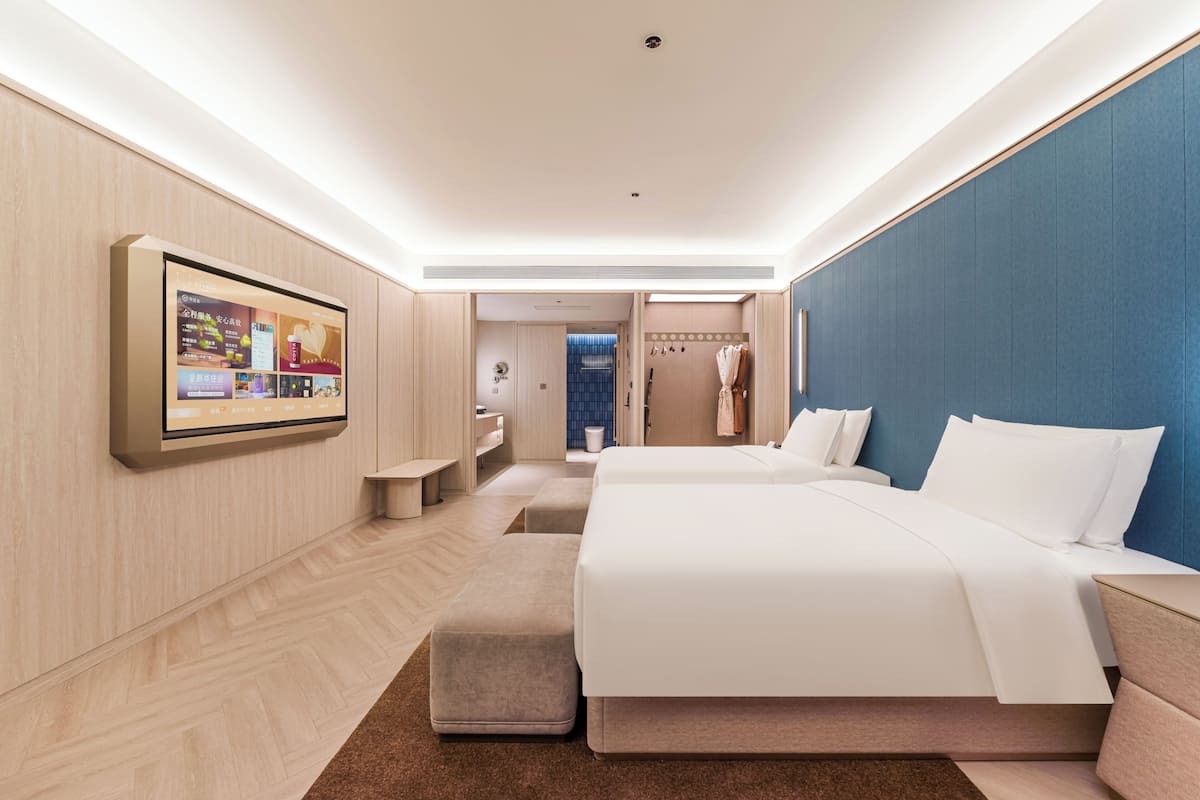 Een moderne hotelkamer met een grote flatscreen televisie, twee bedden, een zithoek en een badkamer zichtbaar door een geopende deur.