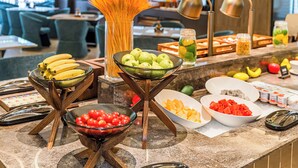 Ein reichhaltiges Buffet mit verschiedenen Früchten und Gemüsen, eine Vase mit Weidenähren und im Hintergrund ein moderner Essbereich.
