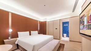 Ein modernes Hotelzimmer mit einem großen Bett, Nachttischen, einer Bank, einem Schreibtisch und einem Fernseher.