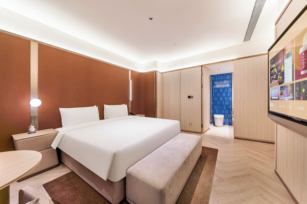Een moderne hotelkamer met een groot bed, nachtkastjes, een bankje, een bureau en een televisie.