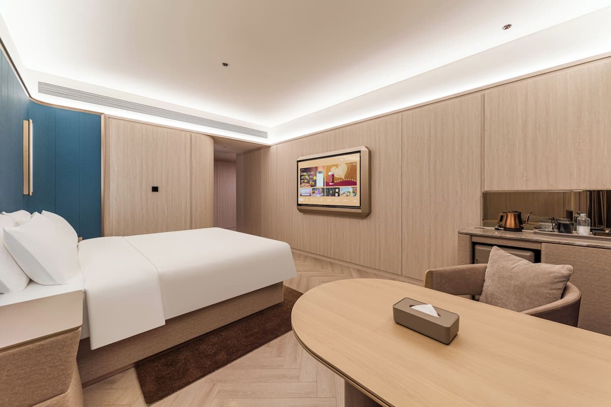 Een moderne hotelkamer met een bed, een bureau, een stoel, een koffiezetapparaat en een tv aan de muur.